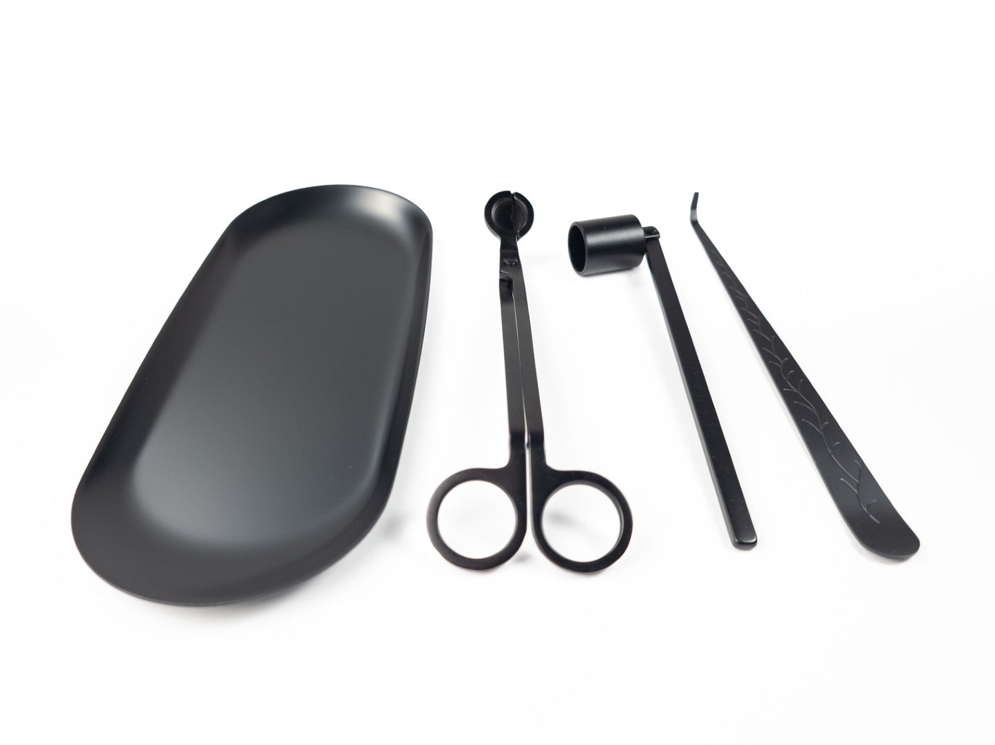 Black candle accessory set displayed on a white background. From left to right: a tray, wick trimmers, a snuffer, and a wick dipper, neatly arranged side by side.