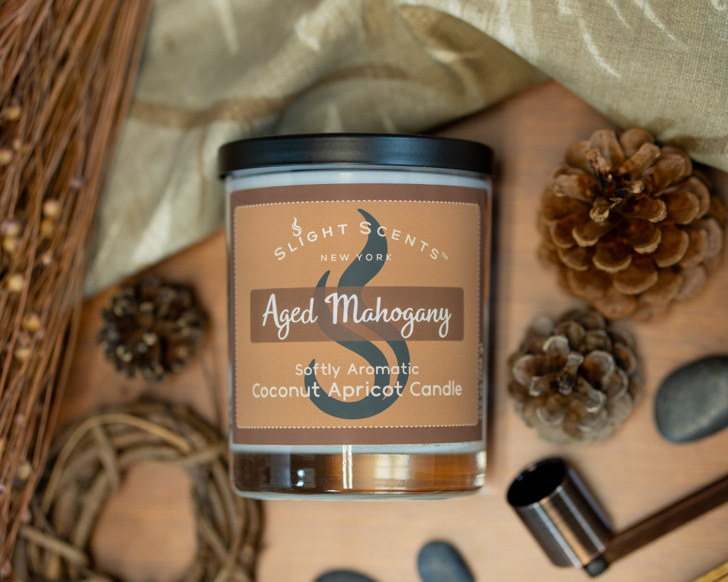 Slight Scents candle labeled 'Aged Mahogany' surrounded by decorative brown elements on a wooden surface.