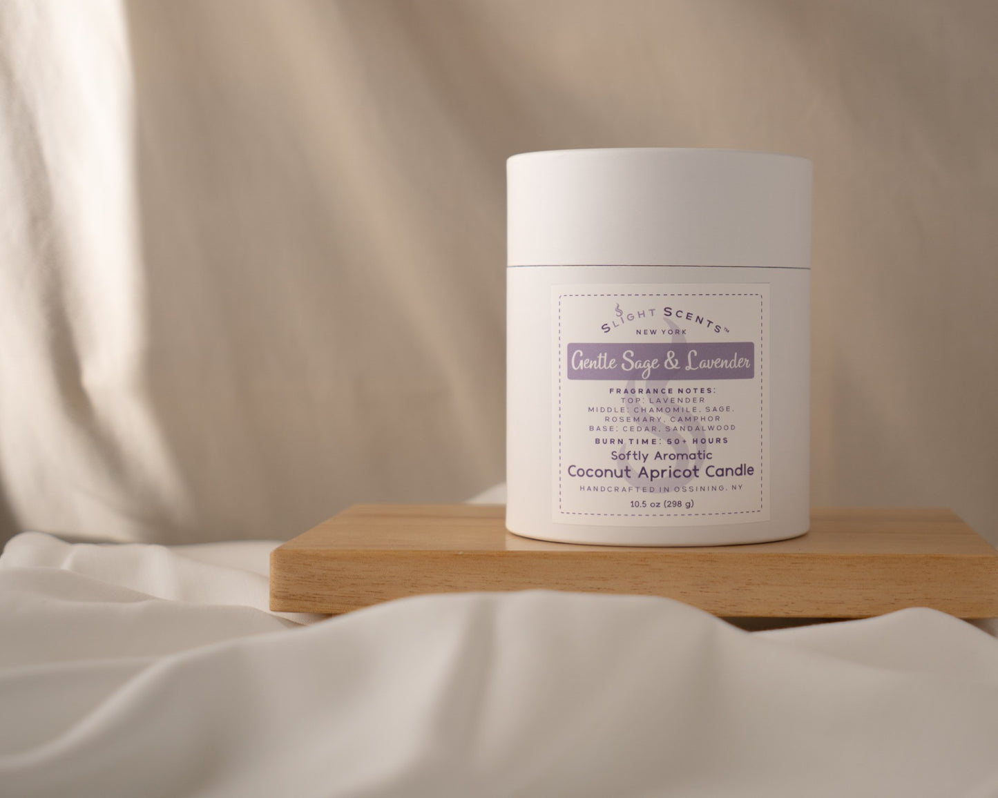 Gentle Sage & Lavender 10.5 oz candle white tube container on a wooden tray against a cloth background.