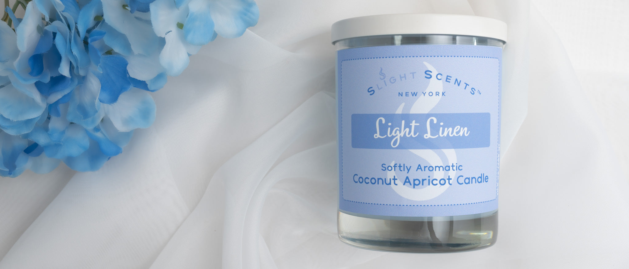 Candle labeled 'Light Linen' with blue flowers on a white cloth background.