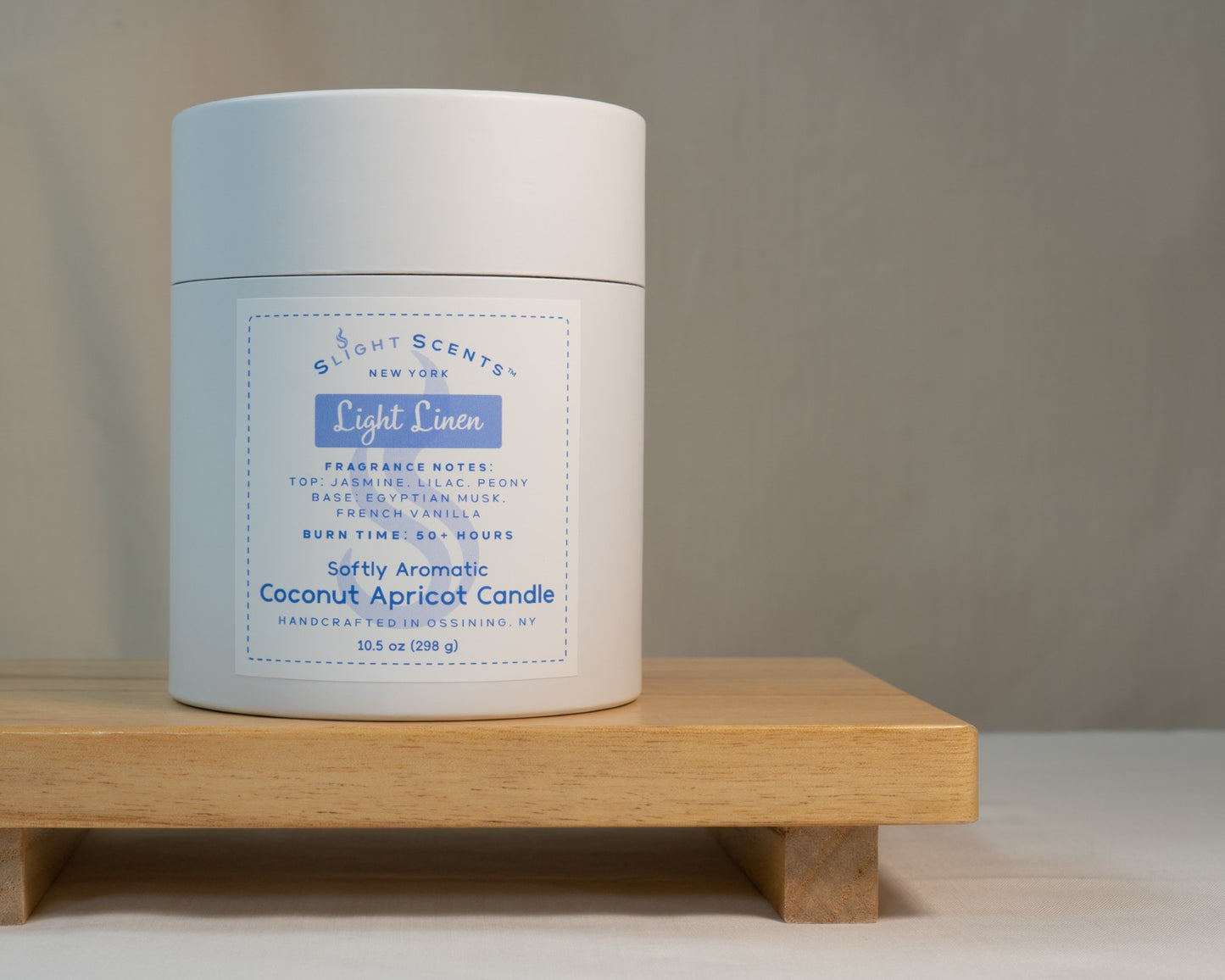 White candle tube container for Slight Scents New York featuring the fragrance Light Linen with notes of jasmine, lilac, peony, Egyptian musk, and French vanilla. Softly Aromatic coconut apricot candle, 10.5 oz, with a burn time of 50+ hours. Handcrafted in Ossining, NY.