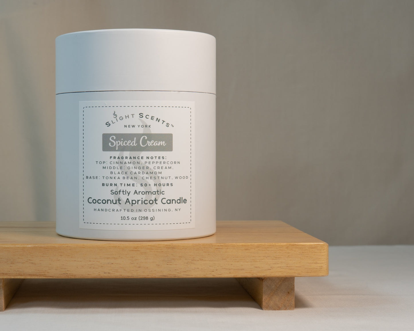 White candle tube container for Slight Scents New York featuring the fragrance Spiced Cream with notes of cinnamon, peppercorn, cream, black cardamom, ginger, tonka bean, chestnut, and wood. Softly Aromatic coconut apricot candle, 10.5 oz, with a burn time of 50+ hours. Handcrafted in Ossining, NY.
