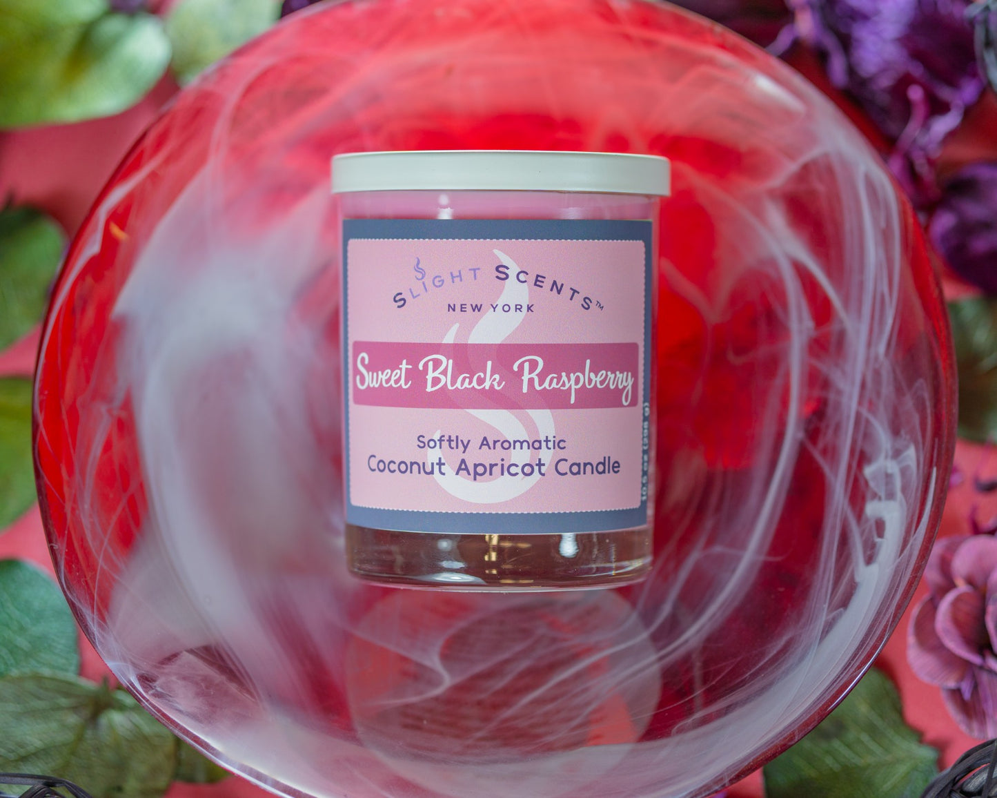 Sweet Black Raspberry Candle in a red bowl surrounded by flowers and leaves.