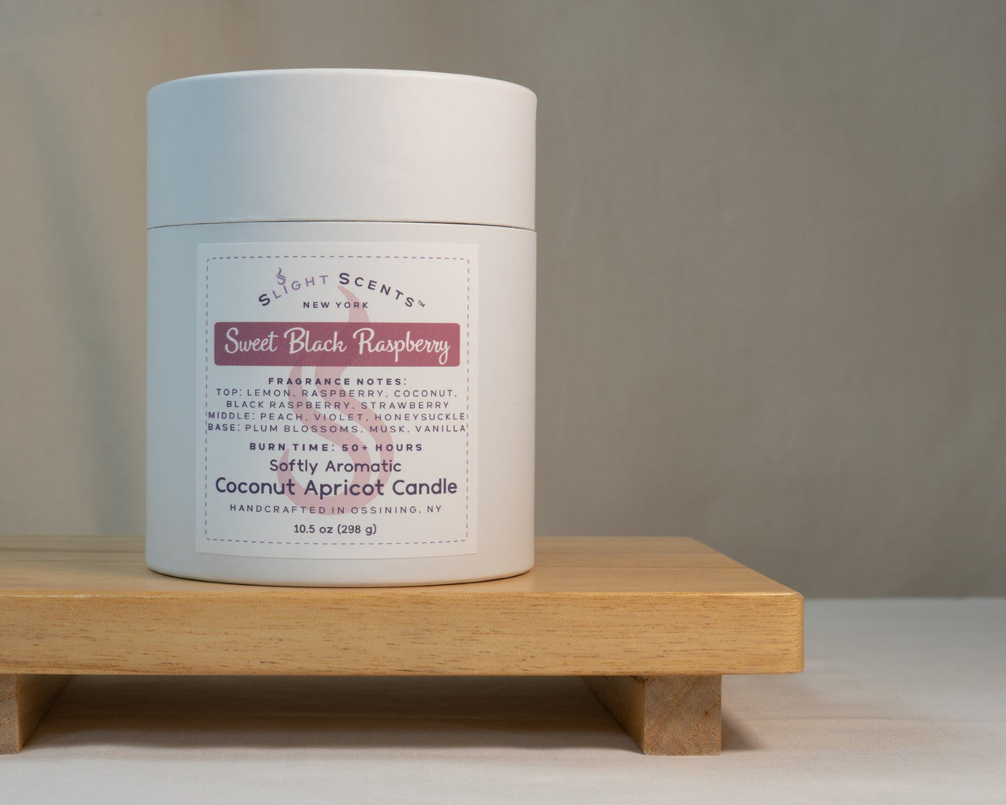 White candle tube container for Slight Scents New York featuring the fragrance Sweet Black Raspberry with notes of lemon, raspberry, black raspberry, strawberry, coconut, peach, violet, honeysuckle, plum blossoms, musk, and vanilla. Softly Aromatic coconut apricot candle, 10.5 oz, with a burn time of 50+ hours. Handcrafted in Ossining, NY.