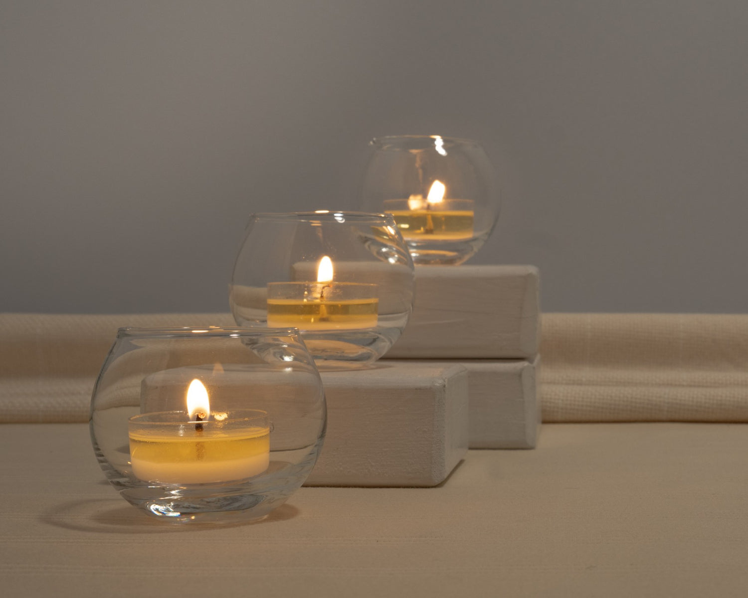 Three glass candle holders with lit tealight candles on a neutral background.