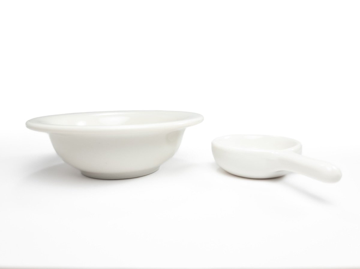 Close-up of a white ceramic bowl for wax melts and a matching tealight holder with a handle, designed for use in a wax warmer.