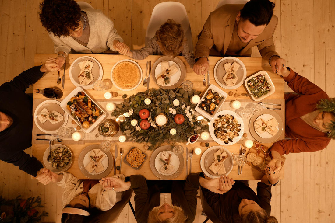 People sitting around a dinner table with a central floral arrangement and candles, set against a wooden wall.