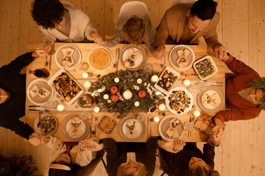 People sitting around a dinner table with a central floral arrangement and candles, set against a wooden wall.