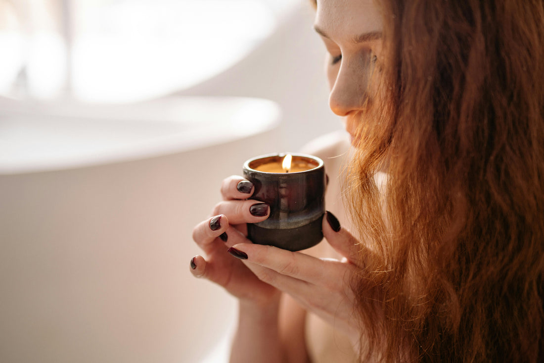 Red haired woman smelling a candle with her eyes closed. 