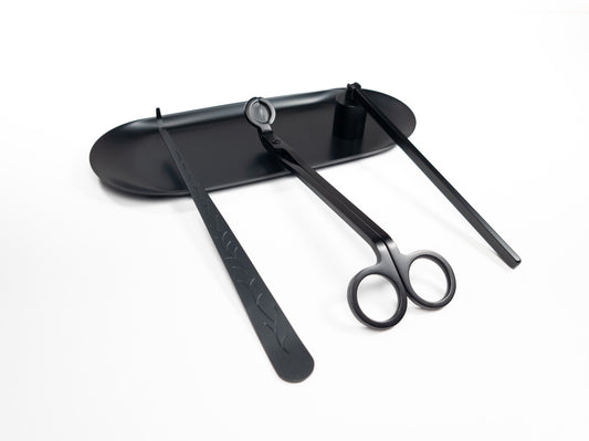 Black candle accessory set on a tray, including a wick dipper, wick trimmer, and snuffer, displayed on a white background.