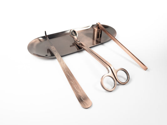 Brushed copper candle accessory set on a tray, including a wick dipper, wick trimmer, and snuffer, displayed on a white background.