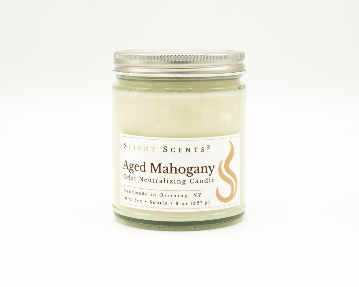 Front view of an Aged Mahogany odor neutralizing candle with white label, undyed wax, and silver metal lid in a glass jar. 