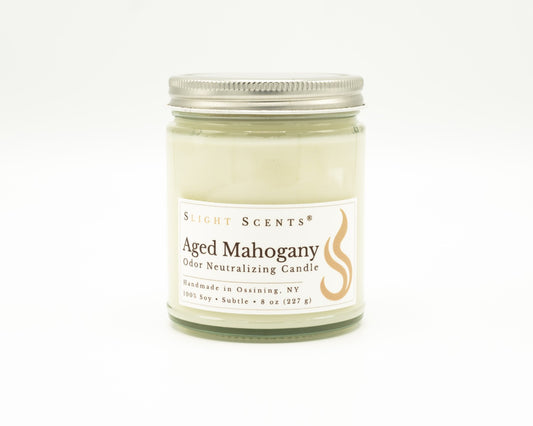 Front view of an Aged Mahogany odor neutralizing candle with white label, undyed wax, and silver metal lid in a glass jar. 