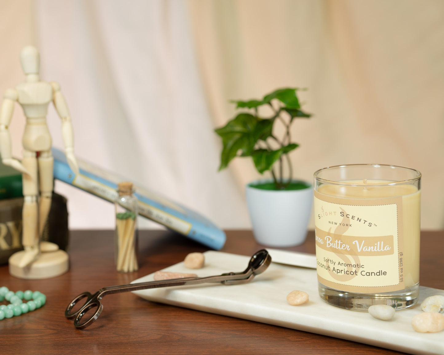 Cocoa Butter Vanilla candle on a marble platter next to wick trimmers, books, plant, and other decorations.