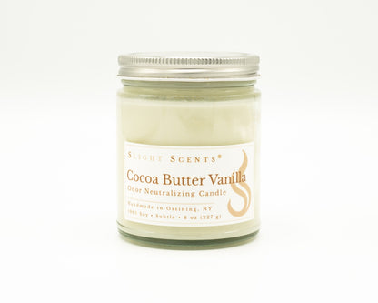 Front view of an Cocoa Butter Vanilla odor neutralizing candle with white label, undyed wax, and silver metal lid in a glass jar. 