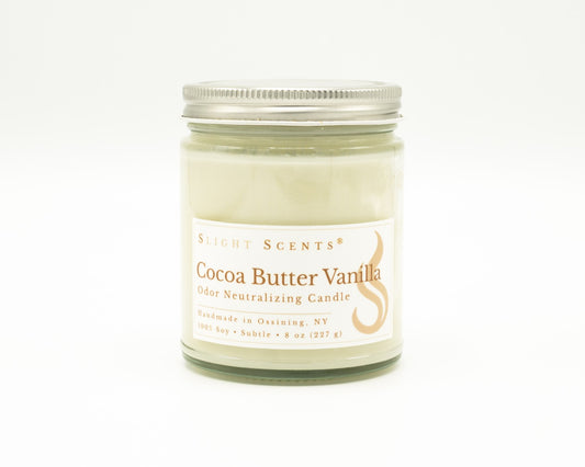 Front view of an Cocoa Butter Vanilla odor neutralizing candle with white label, undyed wax, and silver metal lid in a glass jar. 