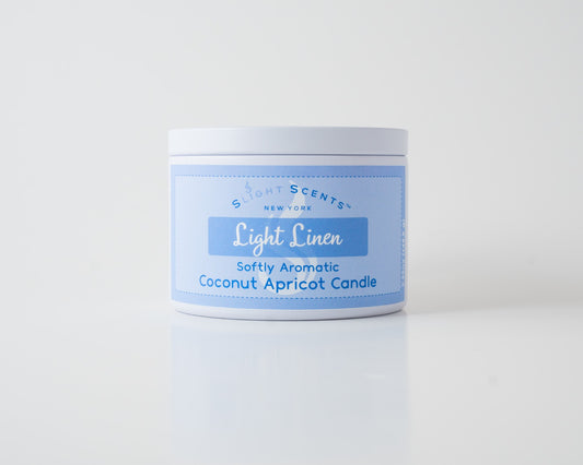 Light Linen Coconut Apricot Candle By Slight Scents New York in a white metal tin on a white background.