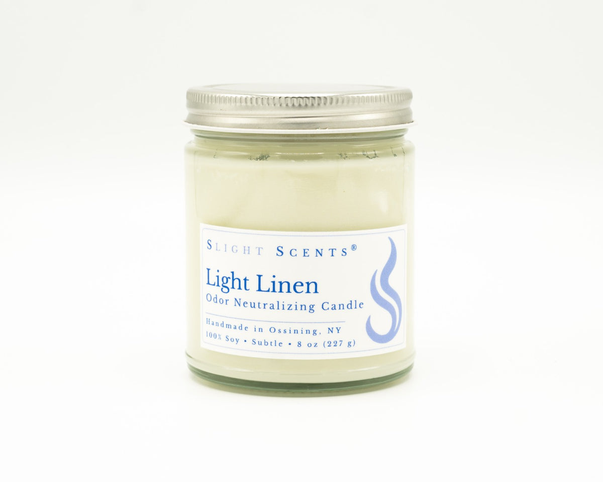 Front view of an Light Linen odor neutralizing candle with white label, undyed wax, and silver metal lid in a glass jar. 