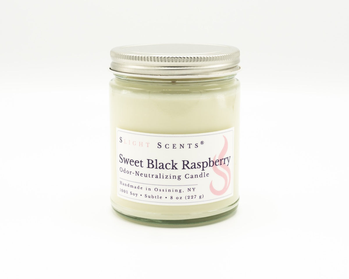 An 8 oz 100% soy candle in a clear glass jar with a silver metal lid, featuring a white label. Slight Scents Sweet Black Raspberry scented odor-neutralizing candle. Handmade in Ossining, NY. 