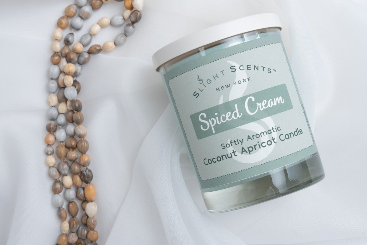 Slight Scents candle labeled 'Spiced Cream' with a beaded necklace on a white cloth background.