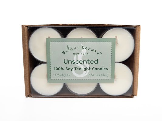 A 12-pack of 100% soy tealights neatly arranged in a cardboard box with a clear plastic cover, showcasing the tealights inside. The packaging displays a green label that says "Slight Scents New York Unscented 100% Soy Tealight Candles." 6.8oz 194g. Box turned on its side.