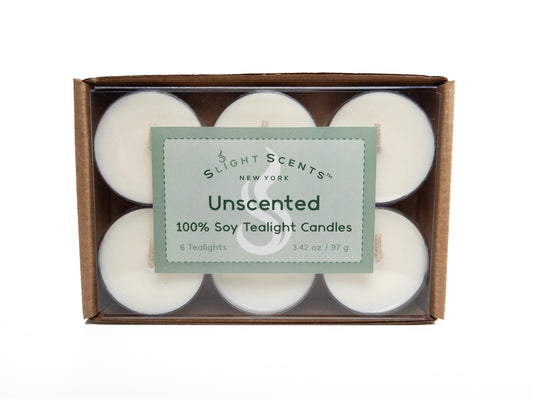 A 6-pack of 100% soy tealights neatly arranged in a cardboard box with a clear plastic cover, showcasing the tealights inside. The packaging displays a green label that says "Slight Scents New York Unscented 100% Soy Tealight Candles." 3.42oz / 97g. Box turned on its side.